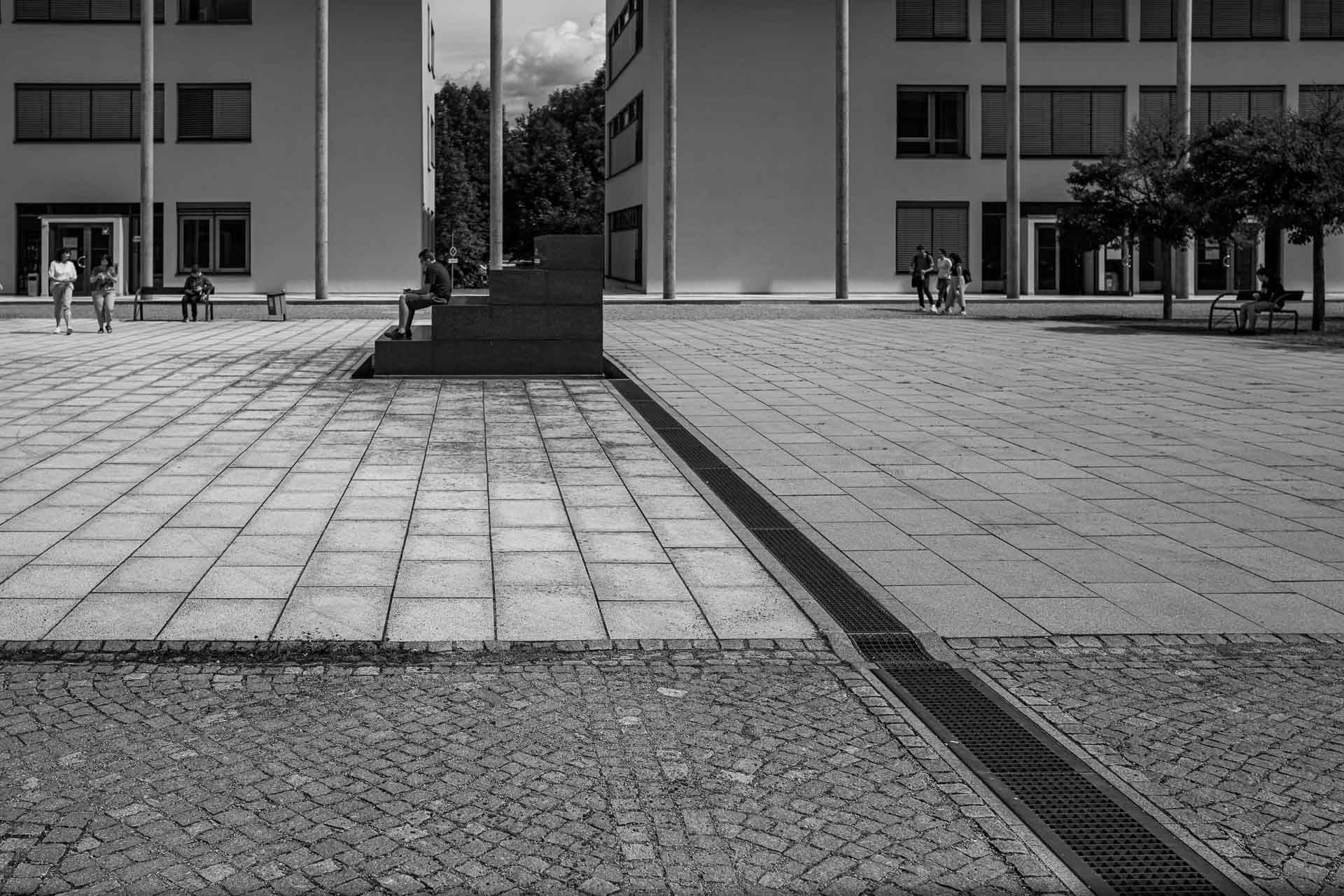 verschiedene Pflaster und Linien führen hin zur Sitztreppe welche ein Student zum Lesen nutzt