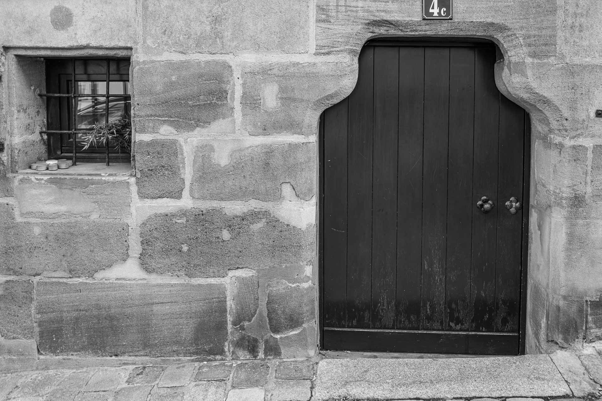 Haus Nr 4c sehr kleine Eingangstür aus Massivholz und links daneben ein quadratisches, vergittertes Fenster